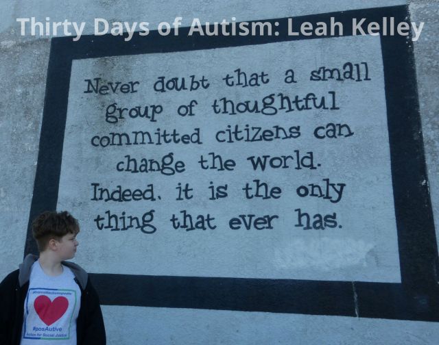 H, wearing his #BoycottAutismSpeaks shirt, is standing in front of an old building. He is looking at the Margaret Mead quote that has been painted on the side. Text reads: "Never doubt that a small group of thoughtful committed citizens can change the world. Indeed, it is the only thing that ever has."